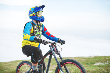 Naklejka premium A young guy sits on a mountain bike atop a mountain, when below the mountains low clouds close-up