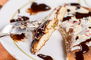 Slice of american pancake topped with chocolate cream and sprinkles on the fork closeup macro