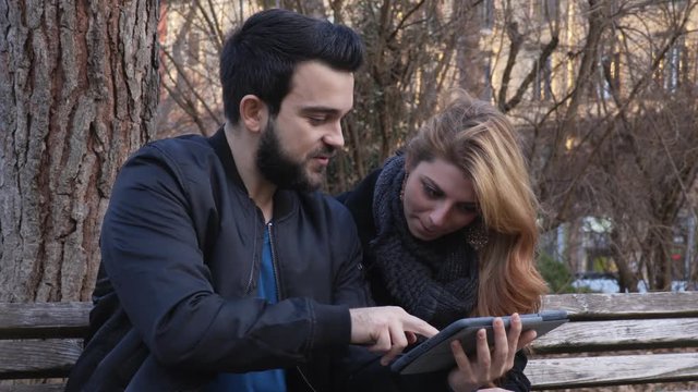 young couple on a bench at the park using tablet 