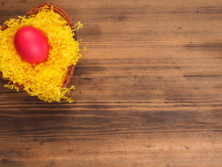 Colored chicken egg on background of bright yellow straw and old wooden table. The view from the top. Creative background for greeting cards, menu or advertising