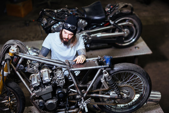 Portrait of tattooed man working in garage customizing motorcycle and repairing broken parts