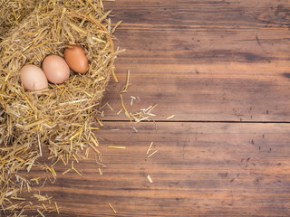 Brown eggs in hay nest. Rural eco background with brown chicken eggs and straw on the background of old wooden planks. Top view. Creative background for Easter cards, restaurant menu or design