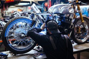 Rückansicht Porträt eines tätowierten Mannes mit Schutzmaske beim Schweißen des Motorradrahmens in der Werkstatt