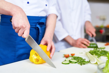 Obraz na płótnie Canvas Trainee cutting fresh yellow pepper during cooking master-class