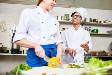 Contemporary chef in uniform consulting his trainee in the kitchen