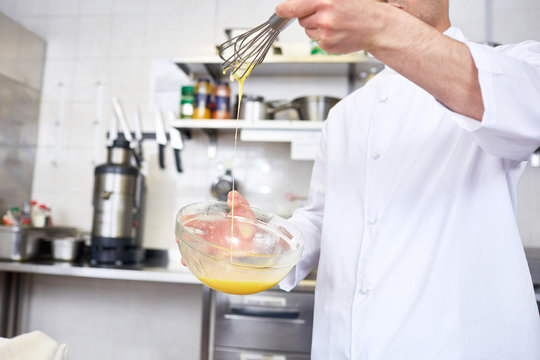 Restaurant chef whisking raw eggs in mixing-bowl