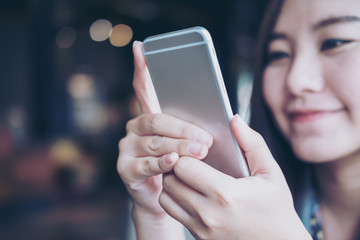 A beautiful Asian girl with smiley face looking and using smart phone in modern cafe with blur bokeh background