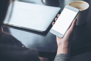 Mockup image of mobile phone with blank white screen with latop and coffee cup on wooden table in cafe