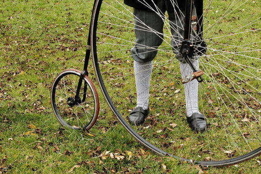An unidentified men with a penny-farthing bicycle in a park with fallen autumn leaves