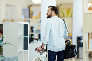 Back view portrait of casual Asian businessman taking bicycle to work in modern creative office