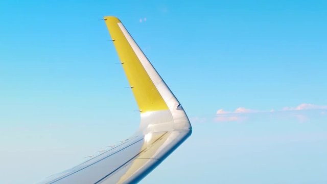 Yellow airliner wing edge against blue sky. Air travel concept. 4K video
