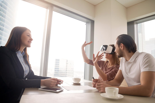 Young woman wearing virtual reality glasses or goggles, couple using head-mounted display for real estate tours, excited by participation effect, virtually discover new flat, buy and sell homes in VR