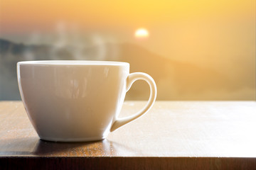Cup of coffee on wooden table in sunrise