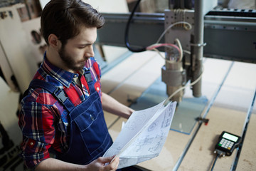 Obraz premium Serious engineer looking at technical sketches by workplace