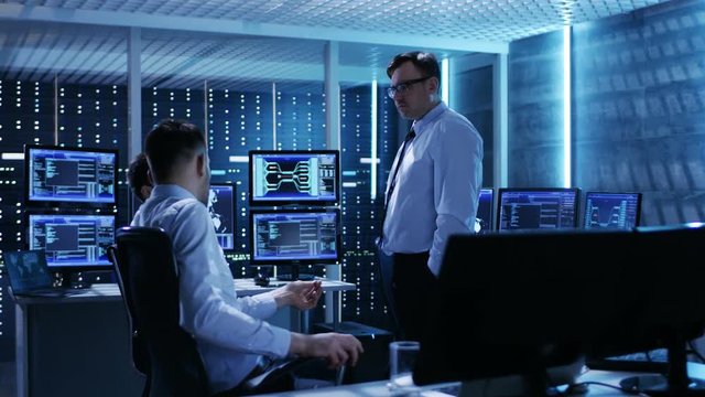 Team of Technical Moderators Have Discussion in Monitoring Room. System Control Room is full of Working Displays and Has Servers Racks.  Shot on RED EPIC-W 8K Helium Cinema Camera.