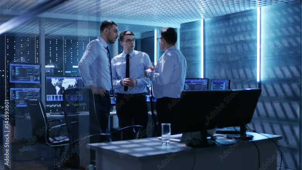 Poster team of technical moderators have active discussion in monitoring room. system control room is full 
