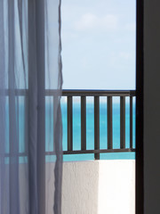 View to the sea from the hotel suite. Open door with white curtains to the balcony. Straight view to the turquoise ocean. Honeymoon and vacation concept image.