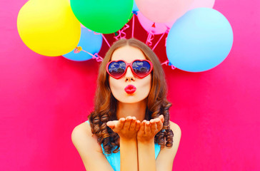 Portrait woman sends an air kiss holds an air colorful balloons on a pink background