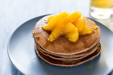 Traditional breakfast: stack of pancakes with orange slices and sweet sauce on blue wooden table. Selective focus