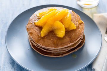 Traditional breakfast: stack of pancakes with orange slices and sweet sauce on blue wooden table. Selective focus