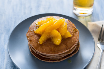 Traditional breakfast: stack of pancakes with orange slices and sweet sauce on blue wooden table. Selective focus