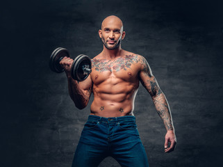 Fototapeta na wymiar Shirtless shaved head, muscular male with tattoos on his chest and arms holds dumbbell.