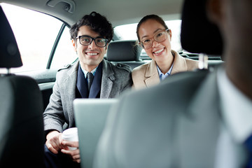 Two young managers looking at camera from backseat of car
