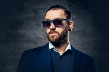 Stylish bearded male in sunglasses over dark grey background.