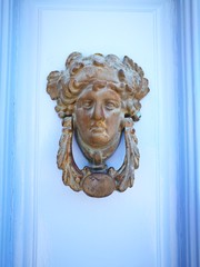 Türklopfer aus Messing mit antiker Figur auf hellblauem Holz einer Haustür im Sommer in der...
