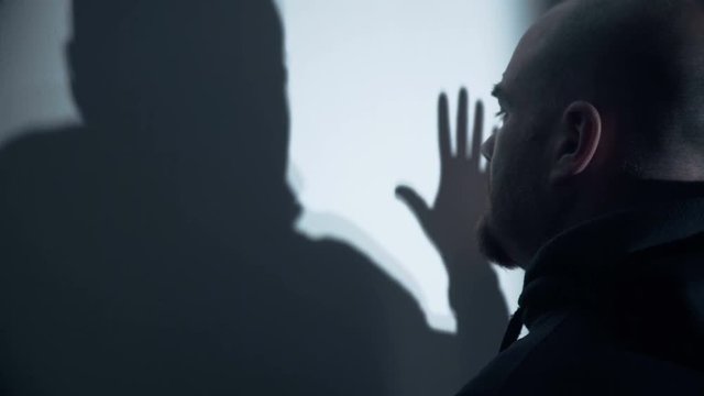 Sad bald man touches his shadow reflected in the wall