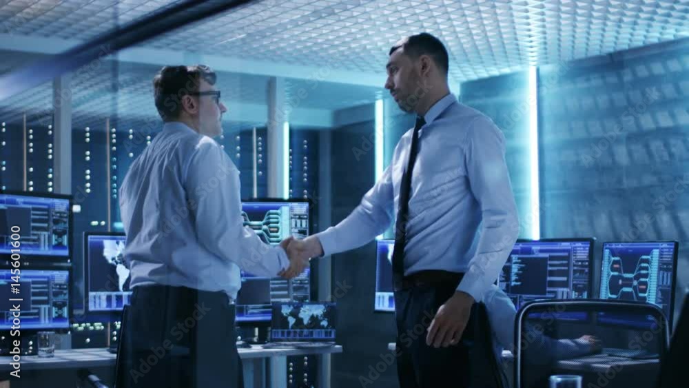 Aufkleber two it engineers have discussion and shake hands in the middle of monitoring room full of working di