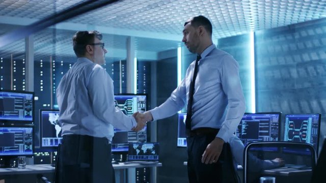  Two IT Engineers Have Discussion and Shake Hands in the Middle of Monitoring Room Full of Working Displays.  Shot on RED EPIC-W 8K Helium Cinema Camera.