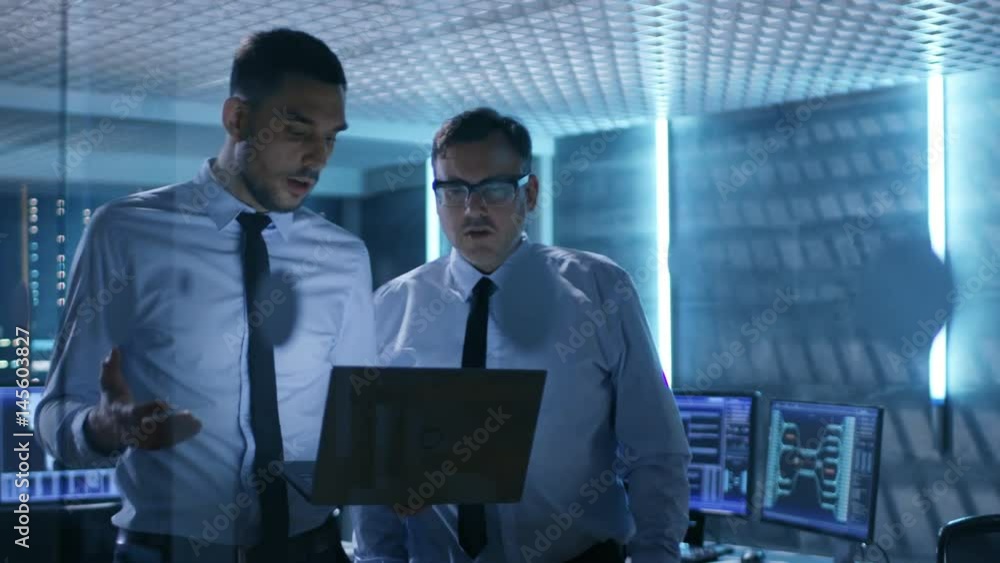Aufkleber two security engineers walking in system control center. they have discussion, one of them holds lap