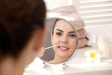 Young woman removing facial hair with wax in front of mirror