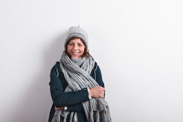 Senior woman in woolen scarf and hat, studio shot.