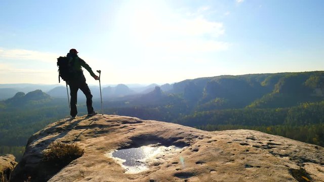 Tourist with medicine crutch above head achieved mountain peak. Hiker with broken leg in immobilizer. Deep misty valley bellow silhouette of happy man with hand in air. Spring morning