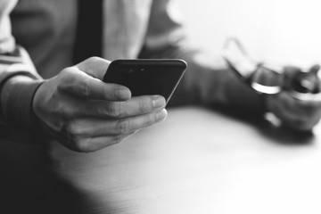 close up of businessman working with mobile phone and eyeglass on wooden desk in modern office