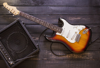 Electric guitar and amplifier connected by cable on wooden background