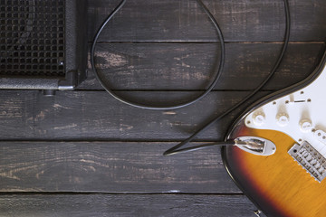 Obraz premium Electric guitar and black amplifier connected by cable on wooden floor