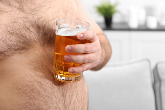 Man holding glass of beer on his big belly at home, closeup