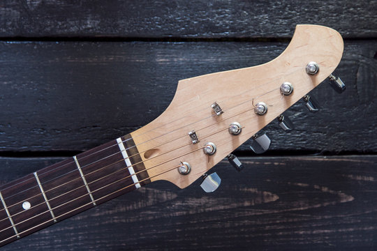 Headstock of electric guitar on wooden background