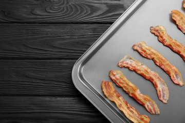 Baking tray with strips of fried bacon on wooden table