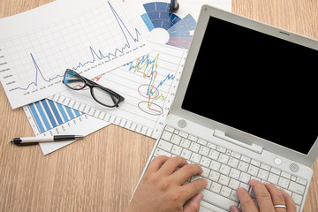 Man's hand typing on laptop computer. Business report, business summary laid on desk.  Business work at home office