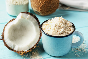 Cup with coconut flour and half of nut on wooden background