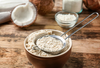 Obraz na płótnie Canvas Bowl with coconut flour and sieve on wooden background