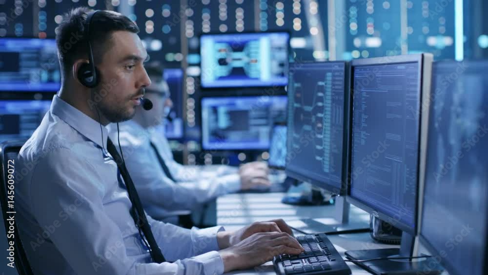 Poster  In the System Control Center Technical Support Team Gives Instructions with the Help of the Headsets. Room is Full of Displays with Various Data on them. Shot on RED EPIC-W 8K Helium Cinema Camera.