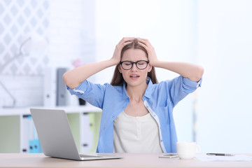 Beautiful young woman suffering from headache while sitting at table in office