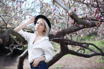 Young blonde girl in hat near magnolia tree on blurred background