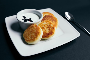 Summer cottage cheese pancakes on white plates on a table with sour cream and berry, closeup, selective focus