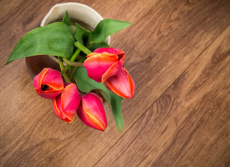 red tulips in a jug on wooden floor view from above